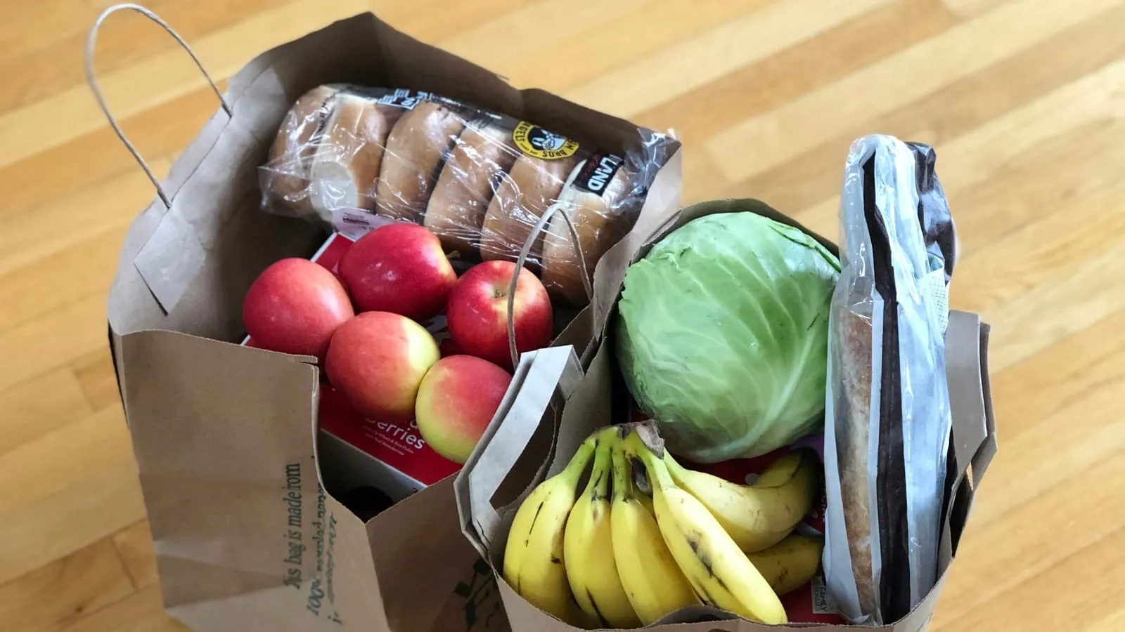 Paper grocery bags filled with apples, bananas, a cabbage and bread